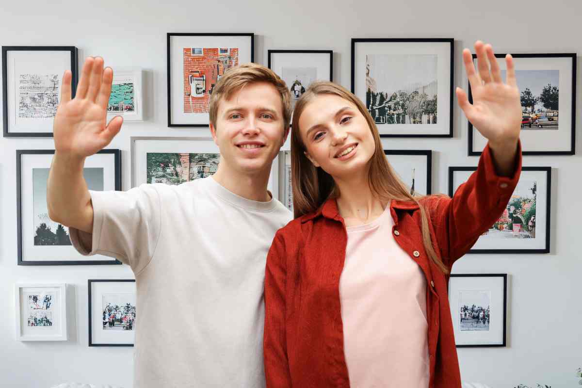 una coppia saluta davanti a una parete piena di quadri appesi