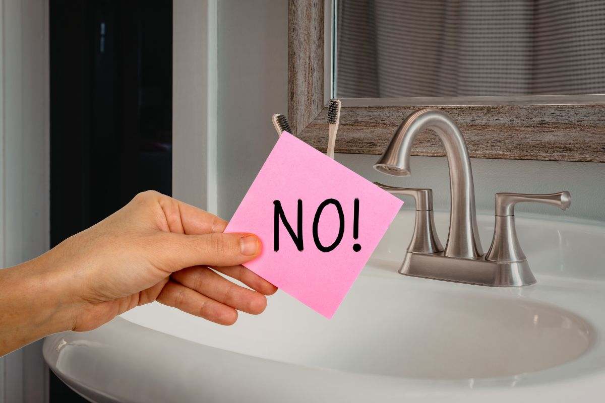 bagno in cui si vede un lavandino e una mano che mantiene un post it con scritta no