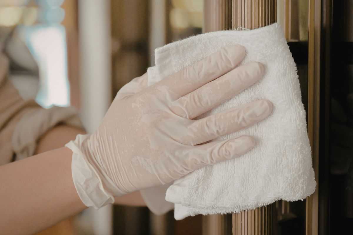 donna che pulisce mobile in legno con pezza e guanti