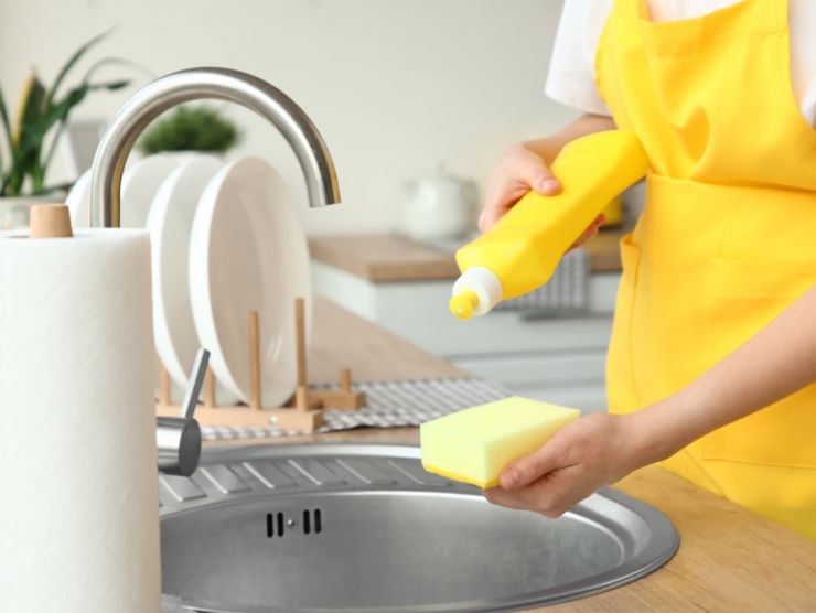 donna che versa del sapone per piatti su una spugnetta