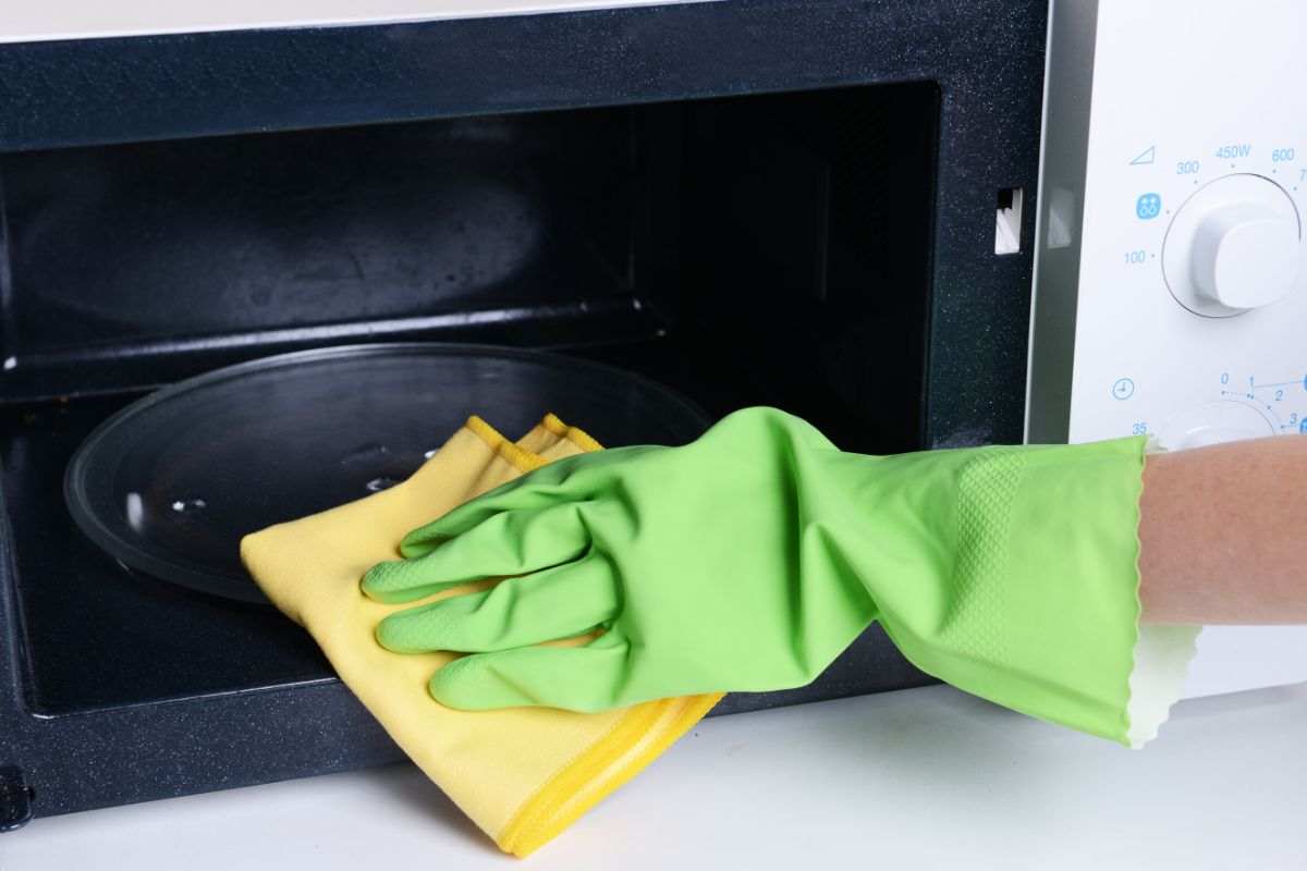 donna che pulisce microonde con guanti e panno